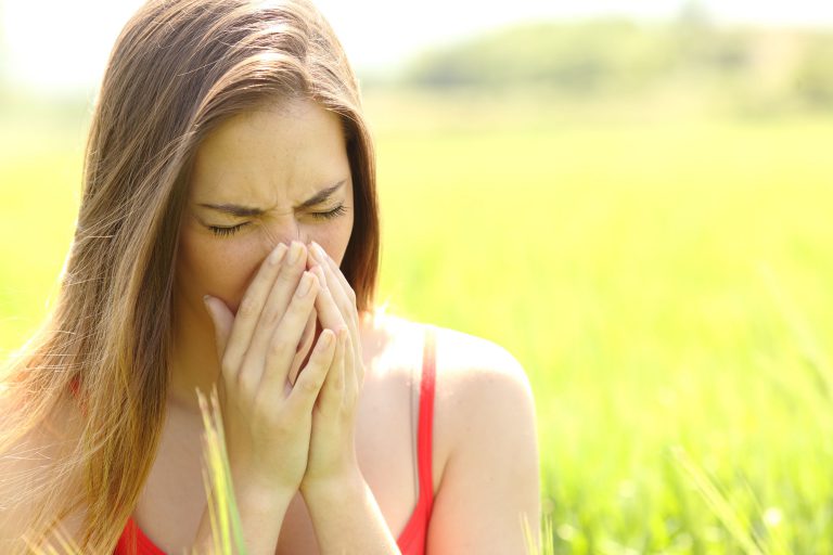 Image of a woman sneezing outside, considering trying acupuncture for her allergies.